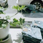 green leafed plant in white pot beside blue denim bottoms on table beside glass panel window